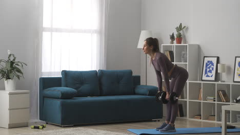 slender-fitness-model-is-training-with-dumbbells-in-hands-standing-in-living-room-of-modern-apartment-healthy-lifestyle-and-wellness-power-training-of-young-woman